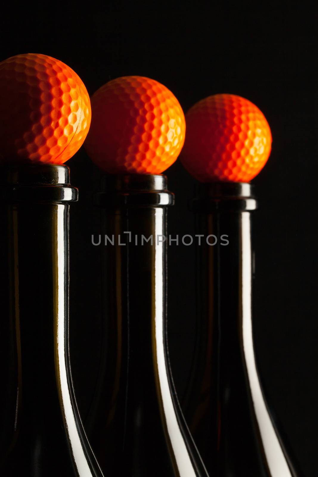 Silhouettes of elegant wine bottles with golf balls on a black background