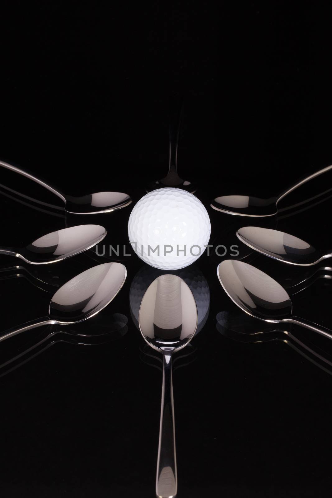 Teaspoons and white golf ball on the black glass desk
