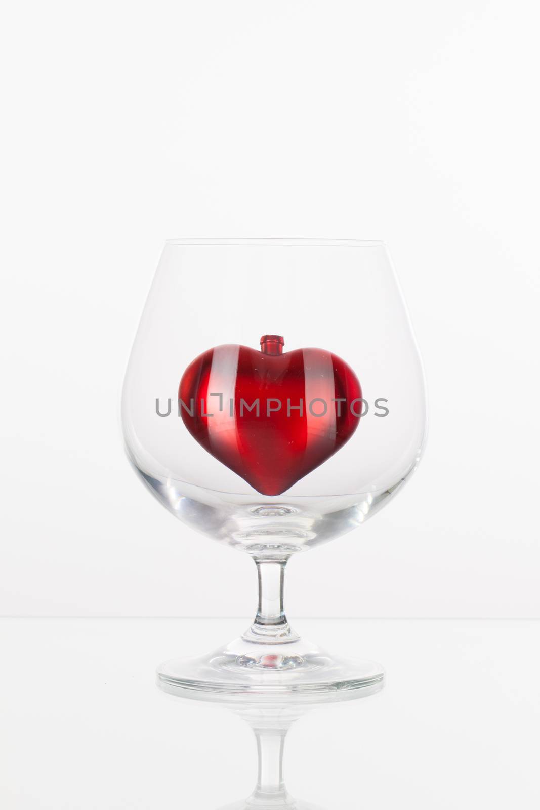 Red heart inside a glass of cognac on a glass plate