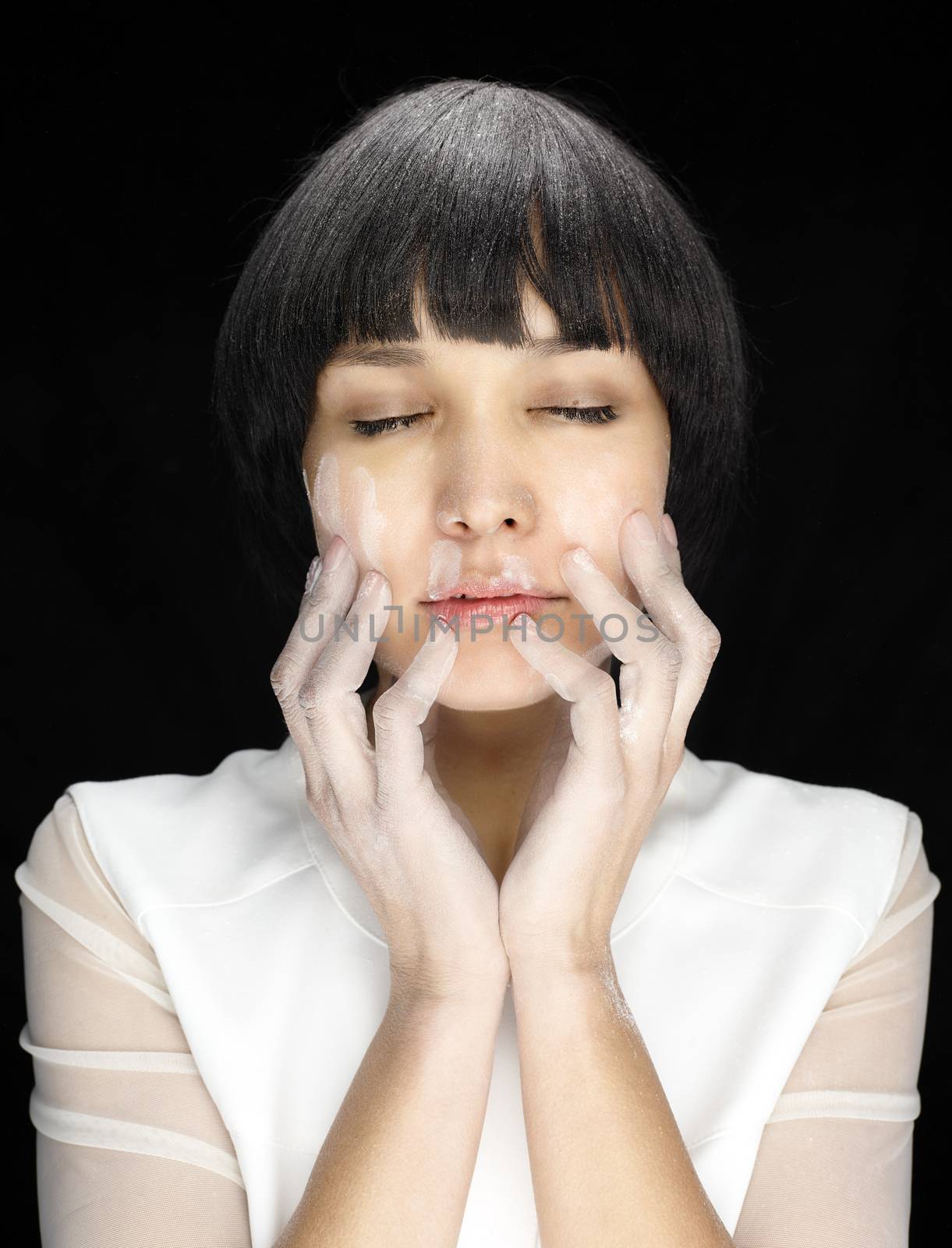 Close up of woman with closed eyes and white prints of flour on face on black background, hands on face