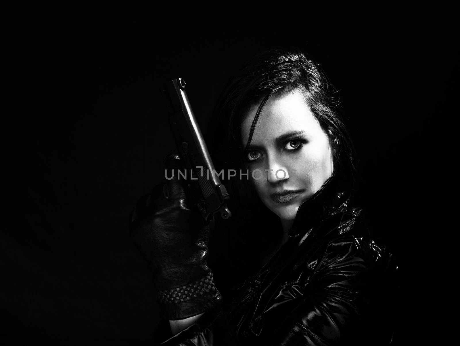 Black and white image of secret agent woman with gun in hand on black background