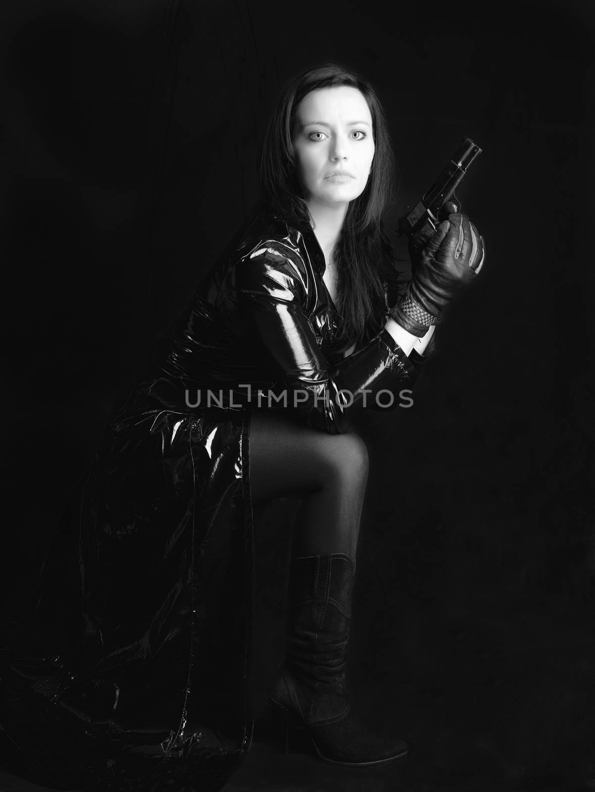 Black and white image of secret agent woman with gun in hand on black background