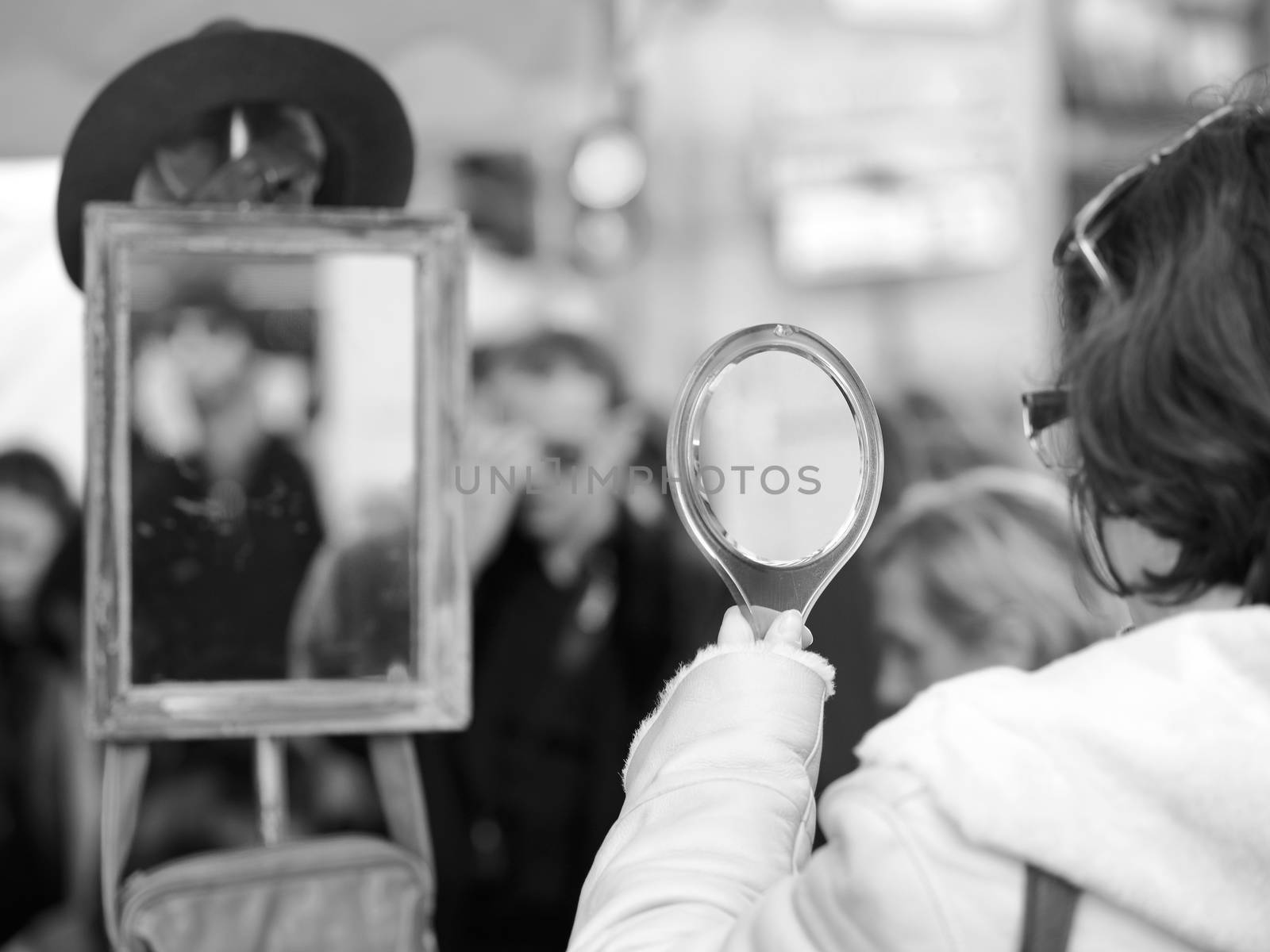 Black and white image of woman looking in handle mirror outdoor
