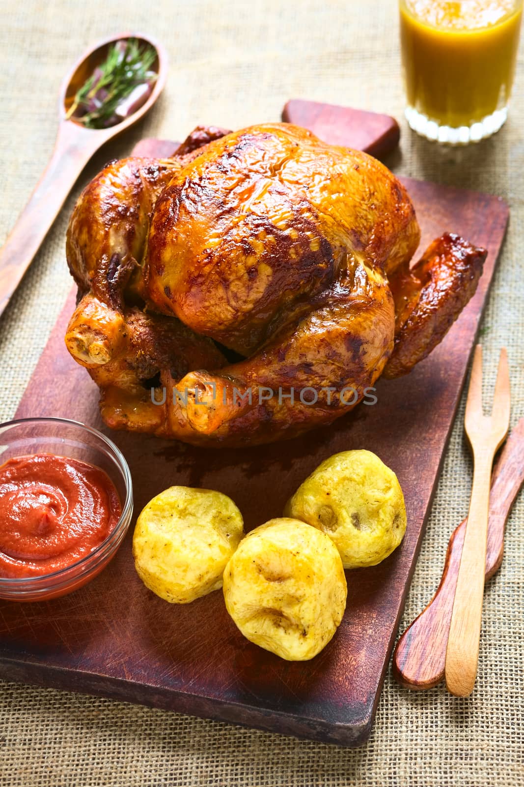Roast Chicken on wooden board with potatoes and ketchup, photographed with natural light (Selective Focus, Focus in the middle of the image)  
