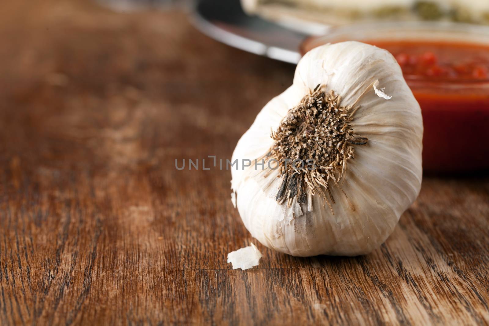 Garlic bulb closeup macro with tomato sauce in the background.  Shallow depth of field.