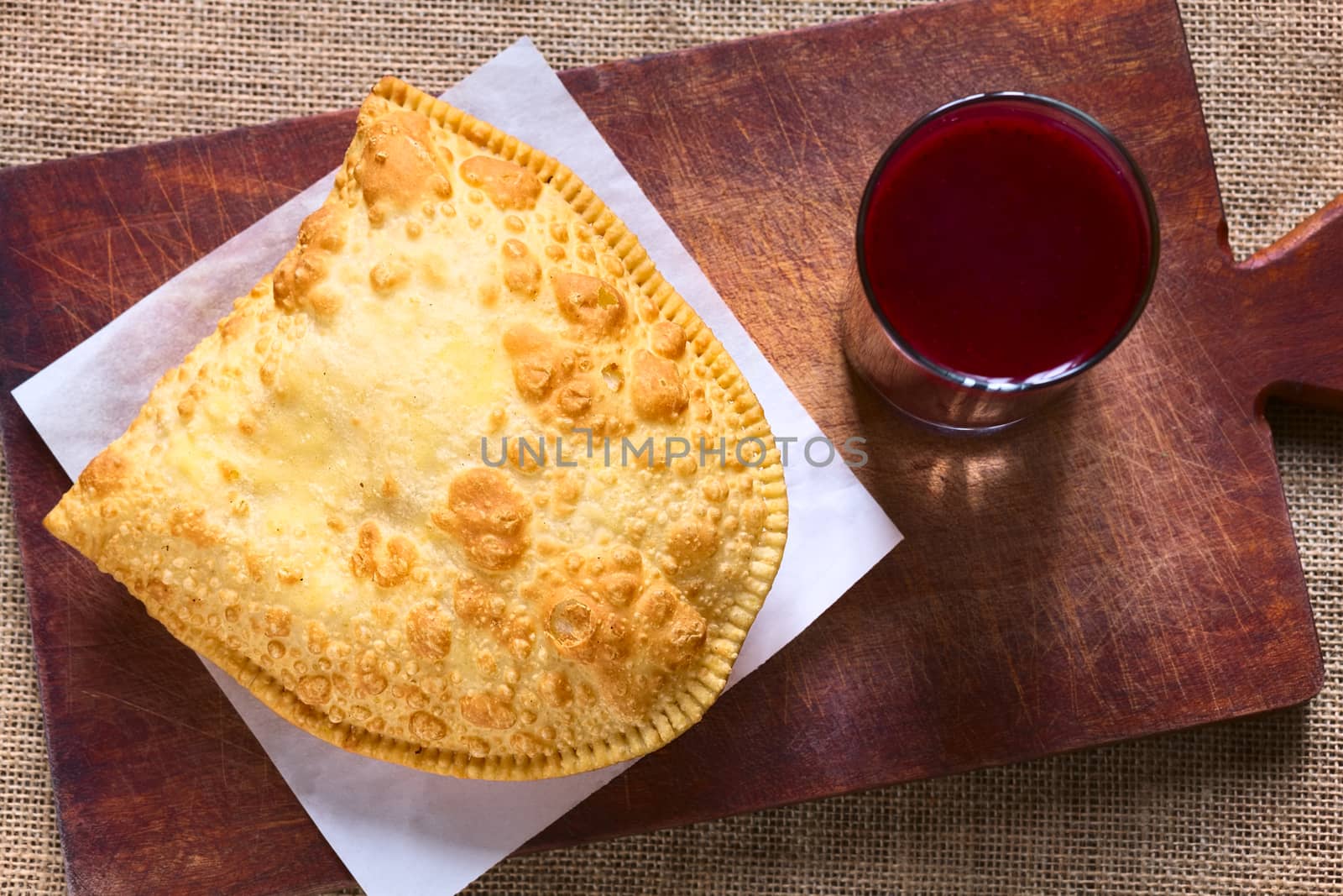 Traditional Bolivian snack called Pastel (deep-fried pastry filled with cheese) served with Api, a purple corn beverage on wooden board, photographed with natural light (Selective Focus, Focus on the pastry)   