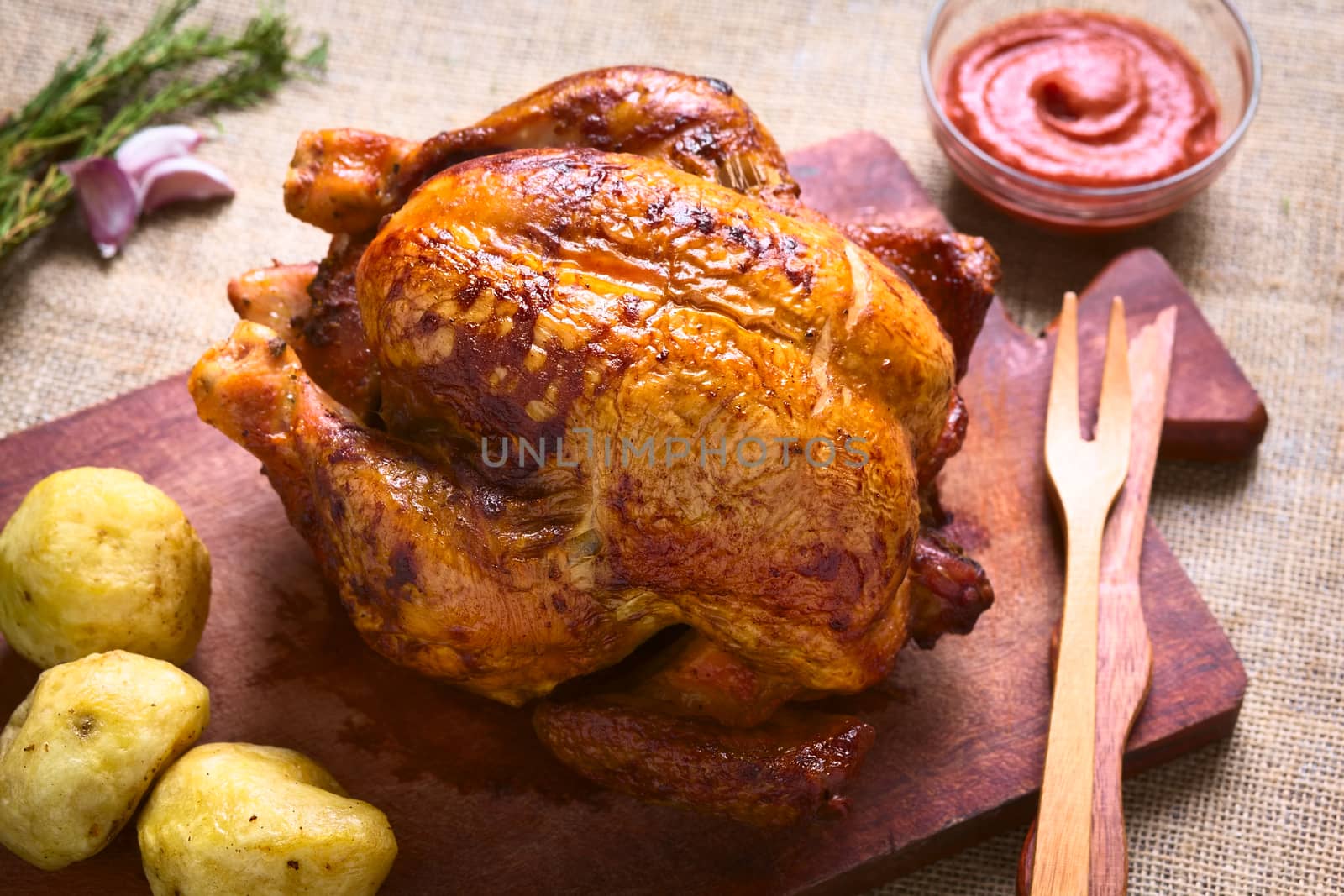 Roast chicken on wooden board with potatoes and ketchup, photographed with natural light (Selective Focus, Focus on the front of the chicken)  