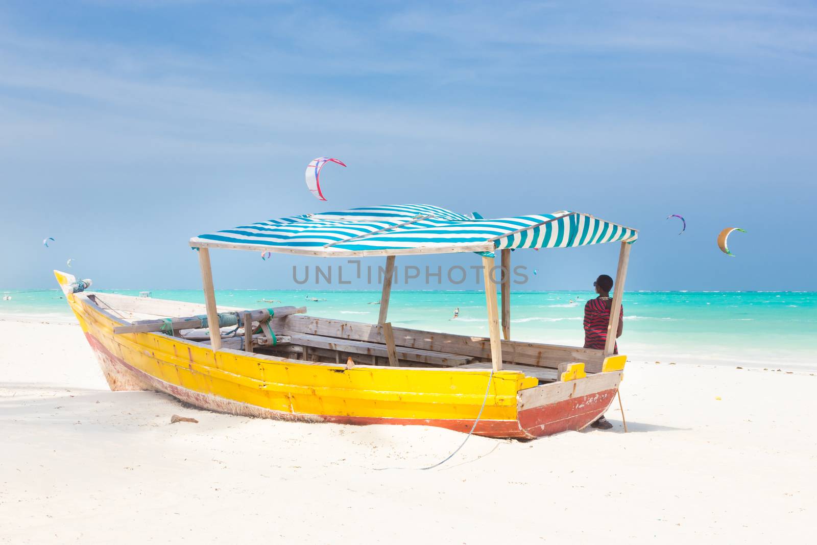 Maasai warrior lounging aroundon traditional colorful wooden boat on picture perfect tropical sandy beach on Zanzibar, Tanzania, East Africa. Kiteboarding spot on Paje beach.