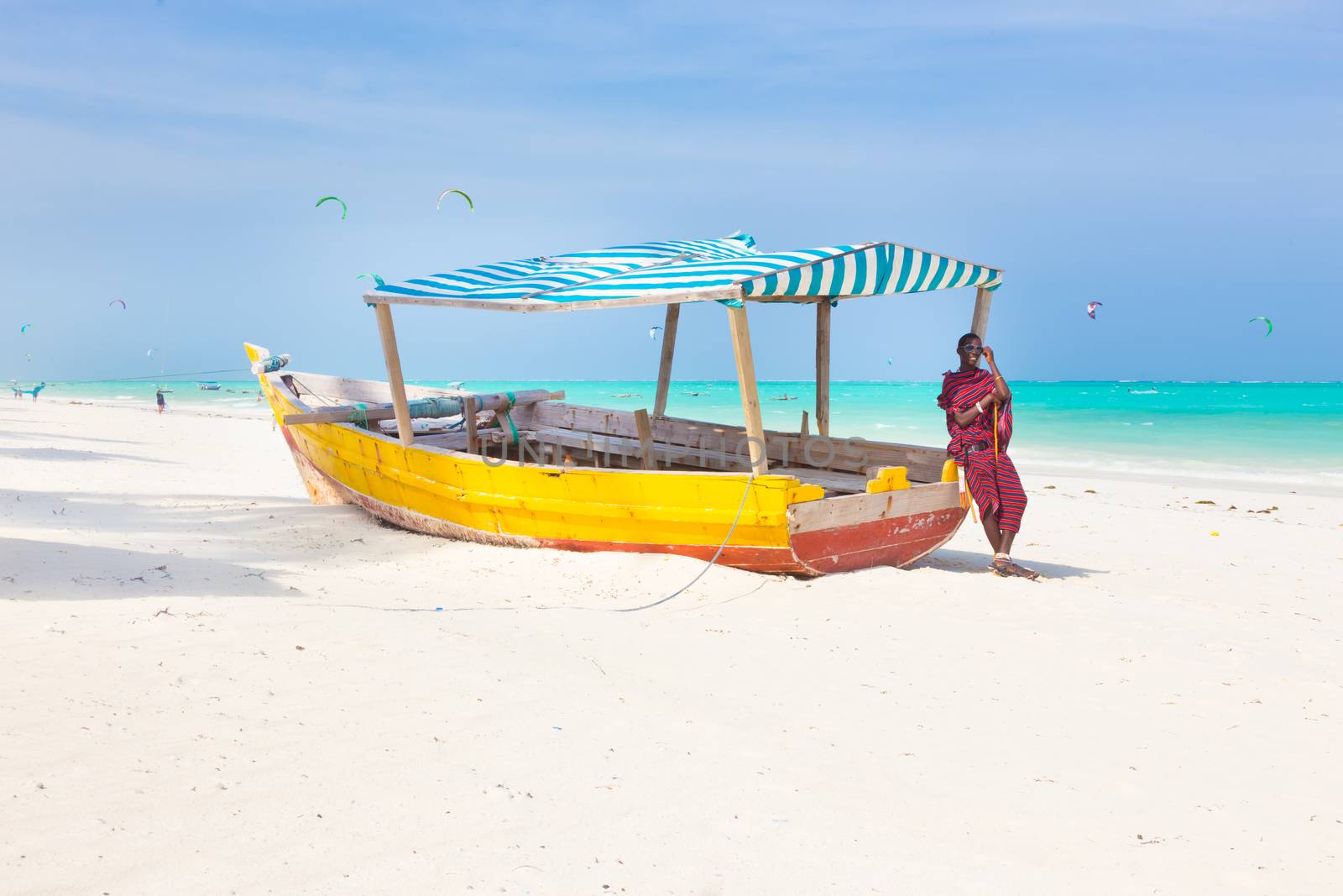 Maasai warrior lounging aroundon traditional colorful wooden boat on picture perfect tropical sandy beach on Zanzibar, Tanzania, East Africa. Kiteboarding spot on Paje beach.