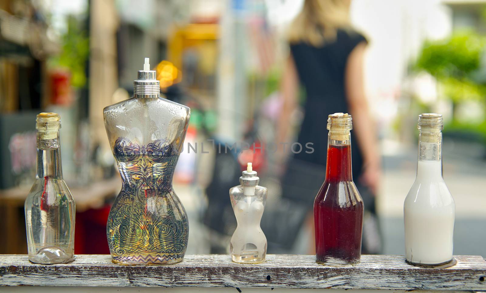 Perfume bottles shaped like the female body with a out of focus woman walking in the background.
