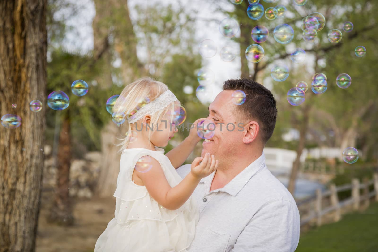 Affectionate Father Holding Cute Baby Girl Enjoying Bubbles Outside at the Park.