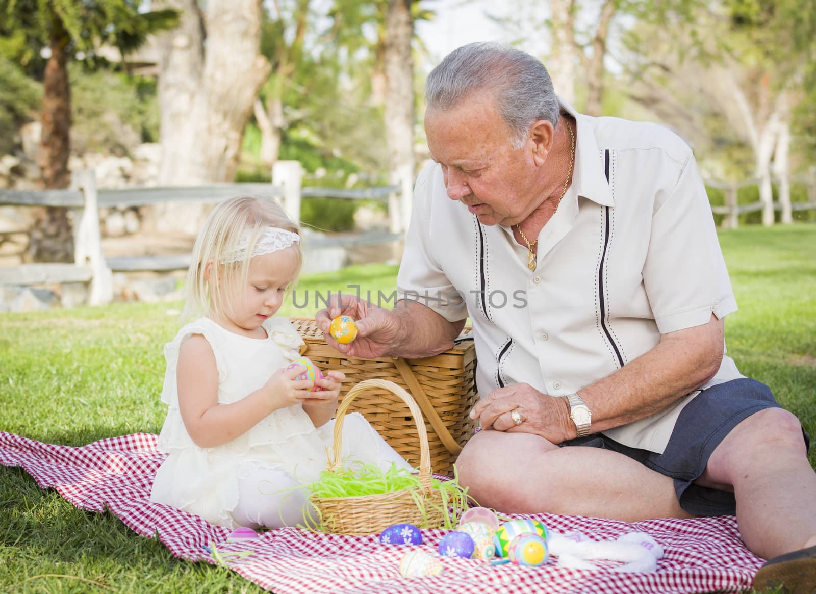 Loving Grandfather and Granddaughter Enjoying Easter Eggs on a Picnic Blanket At Park.