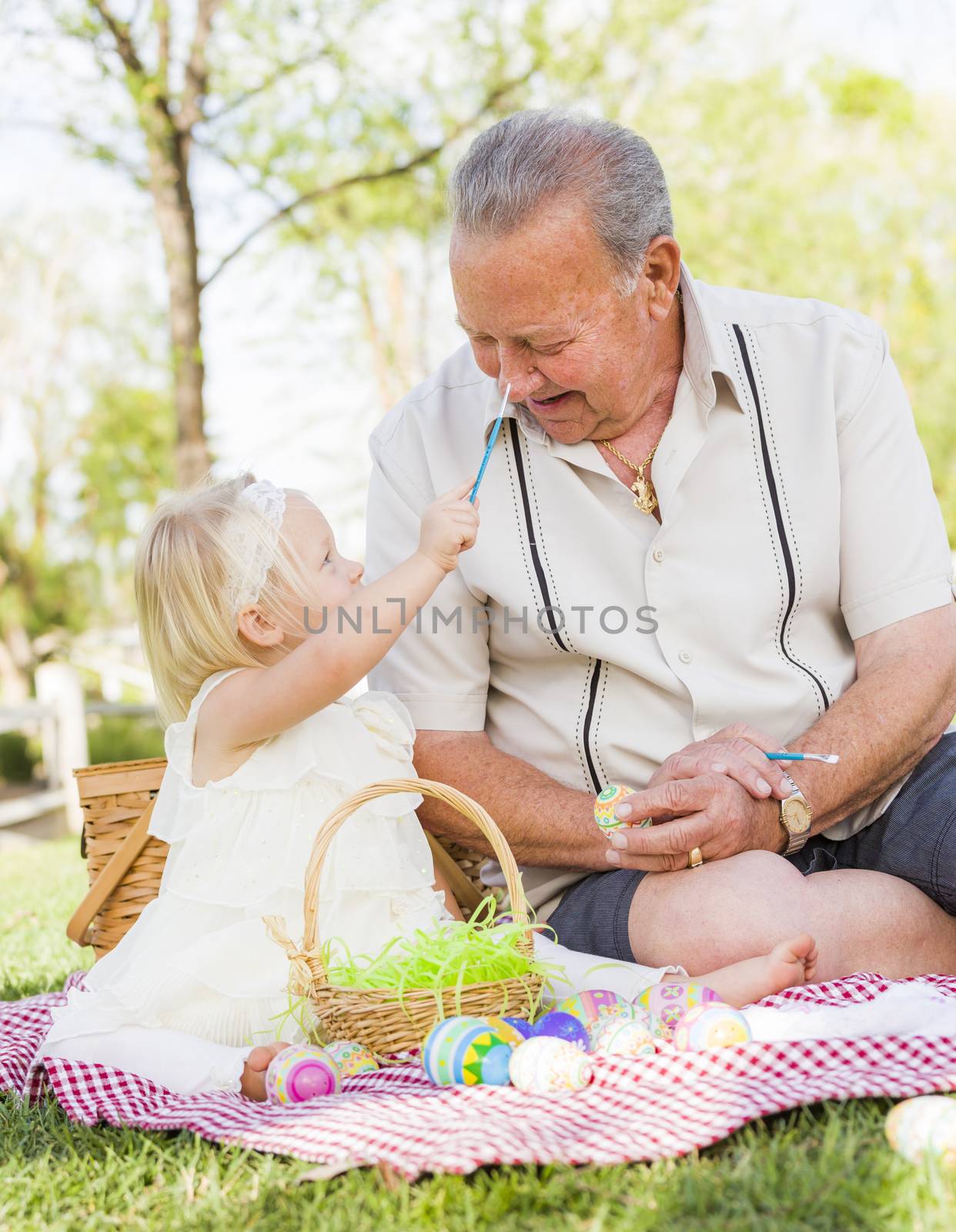 Loving Grandfather and Granddaughter Coloring Easter Eggs Together on Picnic Blanket At The Park.