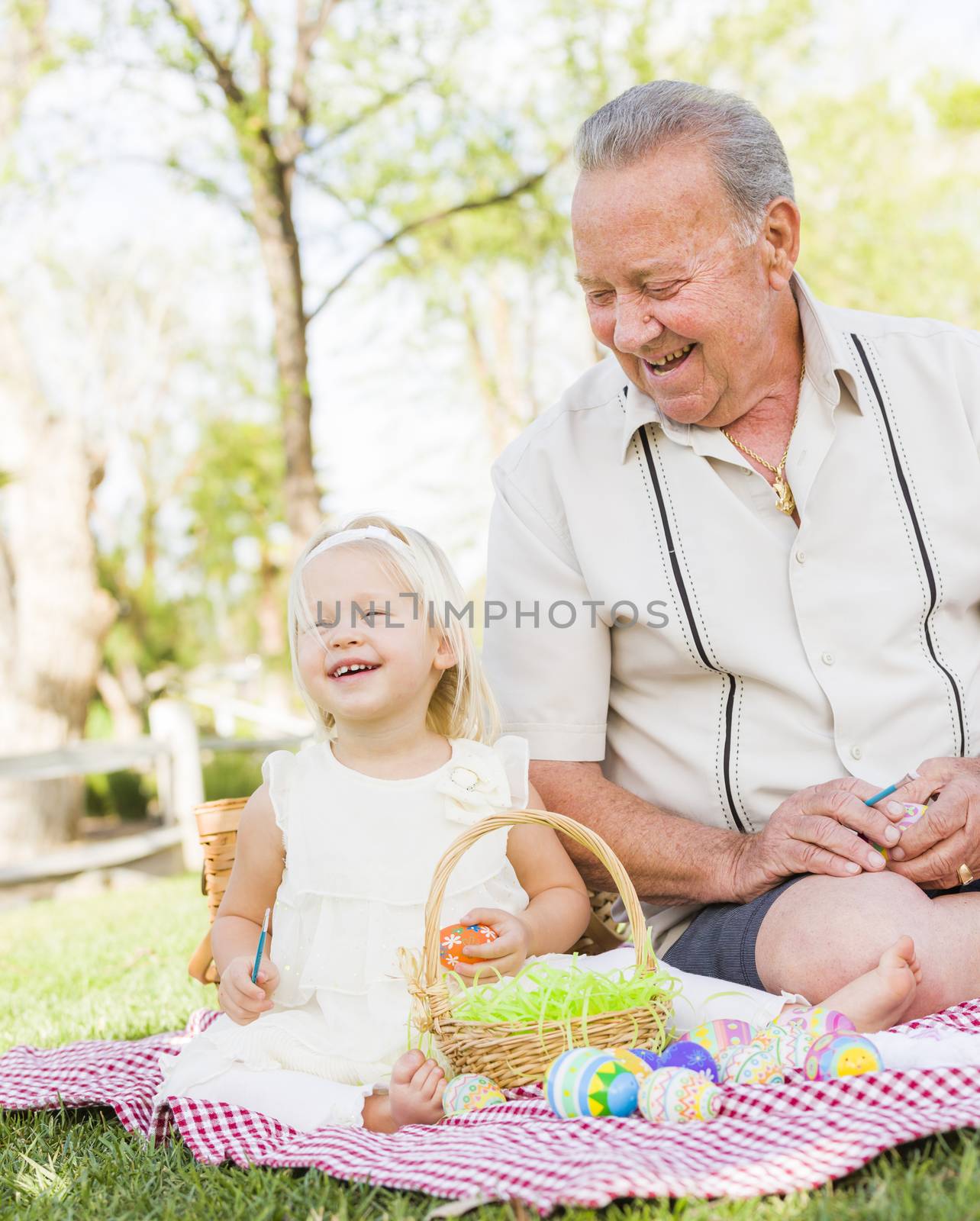 Loving Grandfather and Granddaughter Coloring Easter Eggs Together on Picnic Blanket At The Park.