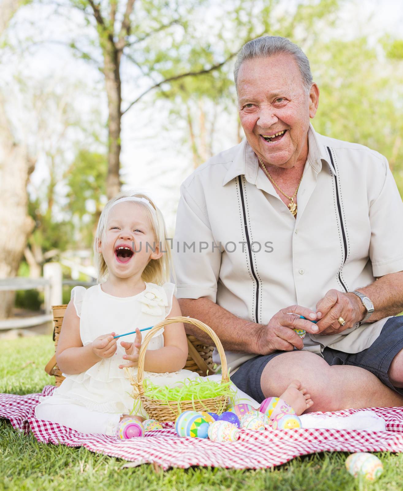 Loving Grandfather and Granddaughter Coloring Easter Eggs Together on Picnic Blanket At The Park.