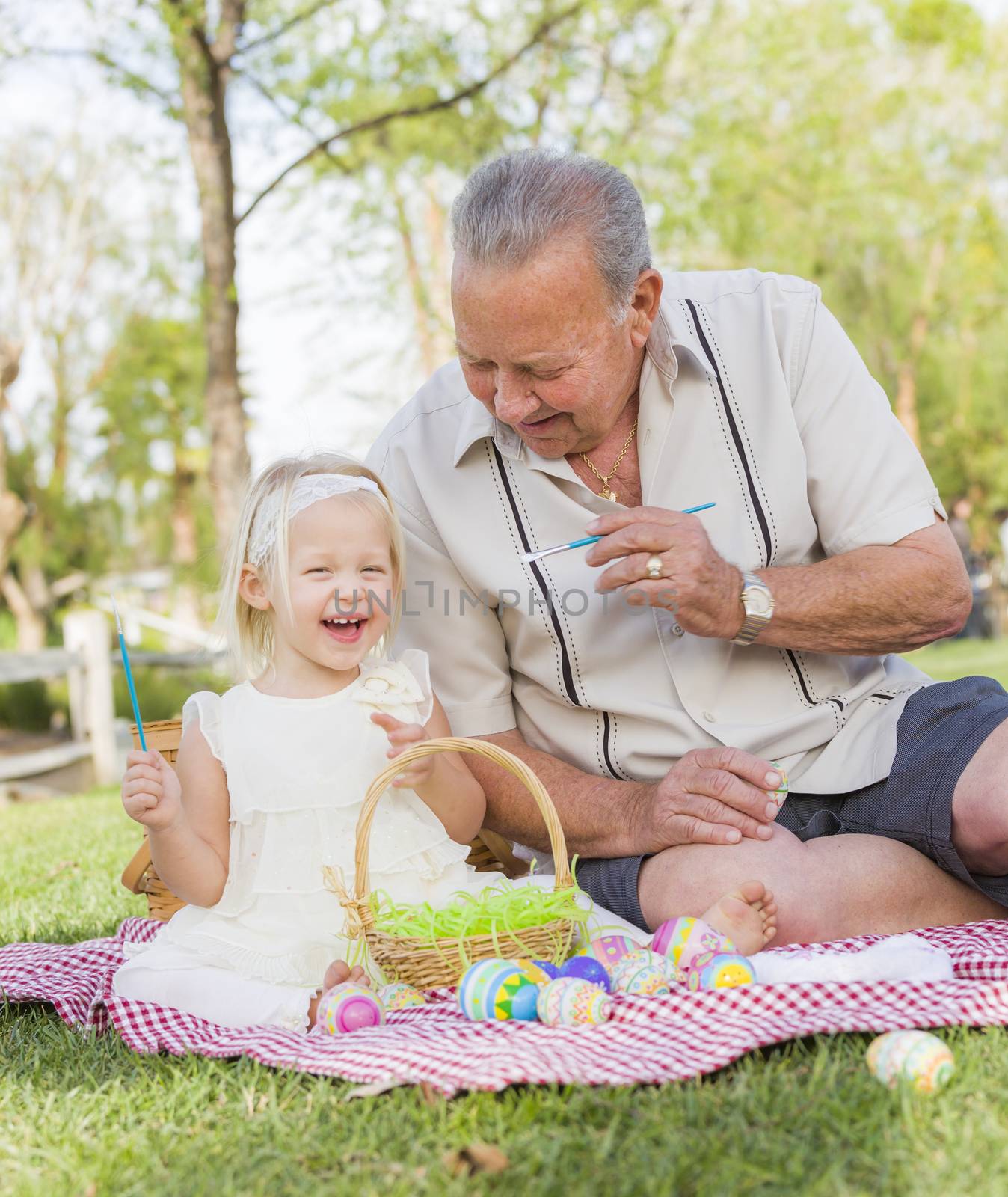 Loving Grandfather and Granddaughter Coloring Easter Eggs Together on Picnic Blanket At The Park.