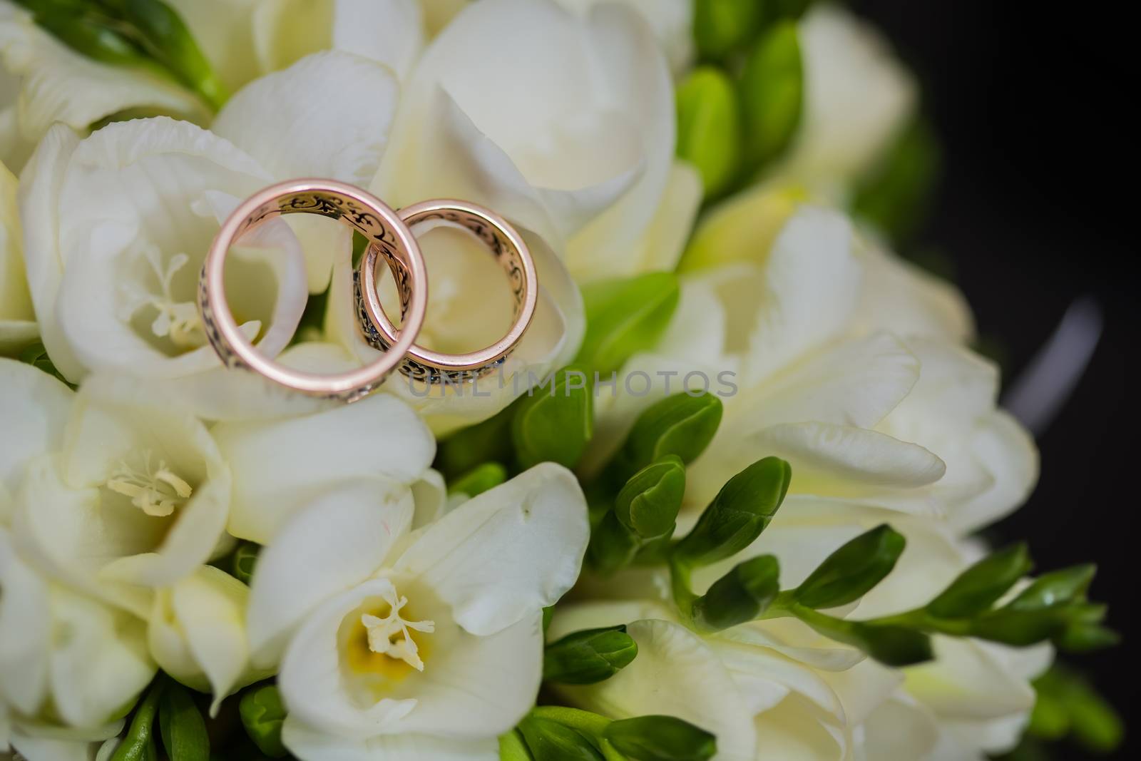 Two wedding rings in infinity sign with bouquet on black background. Love concept.