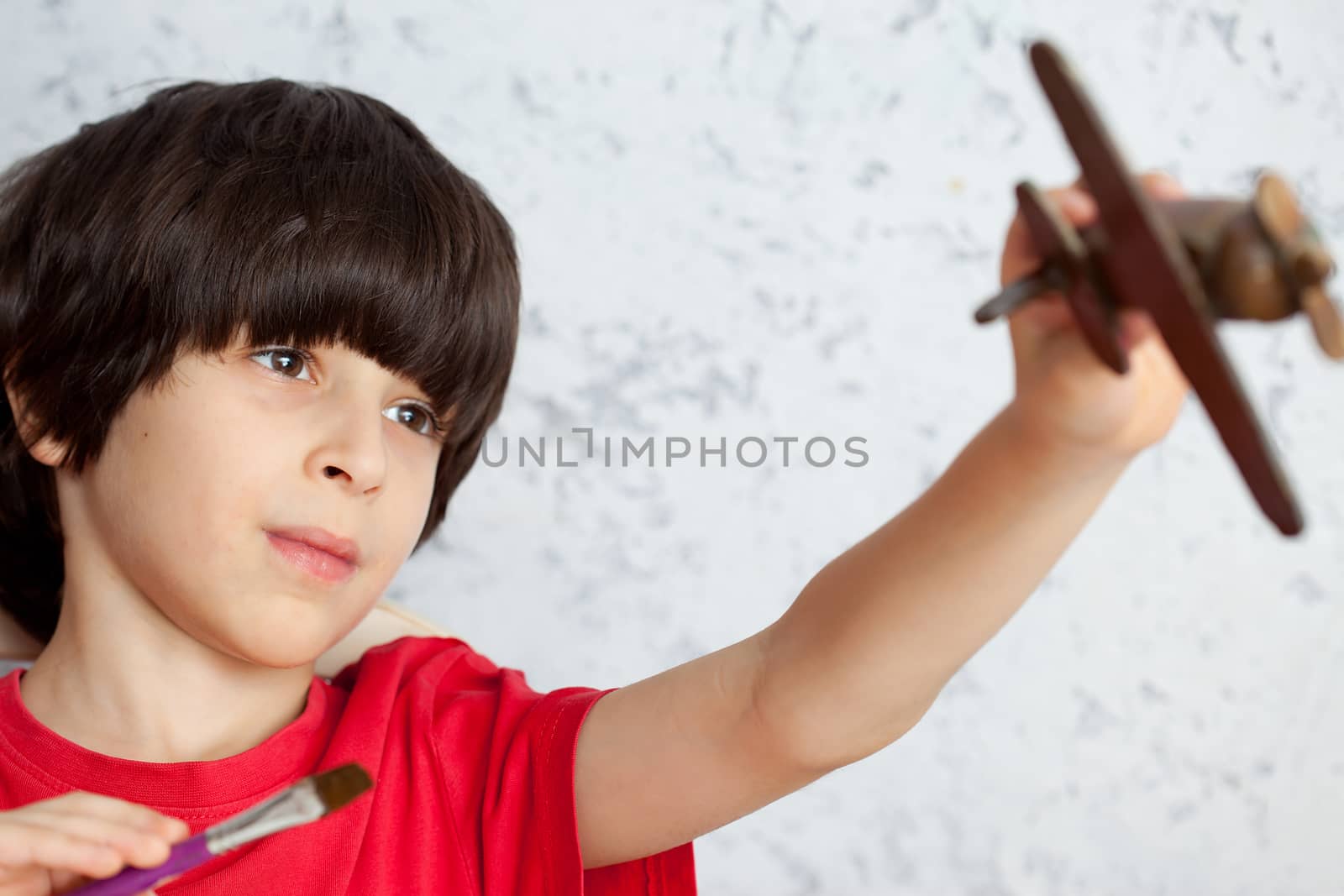 portrait of a boy in a red shirt with a wooden plane and brush