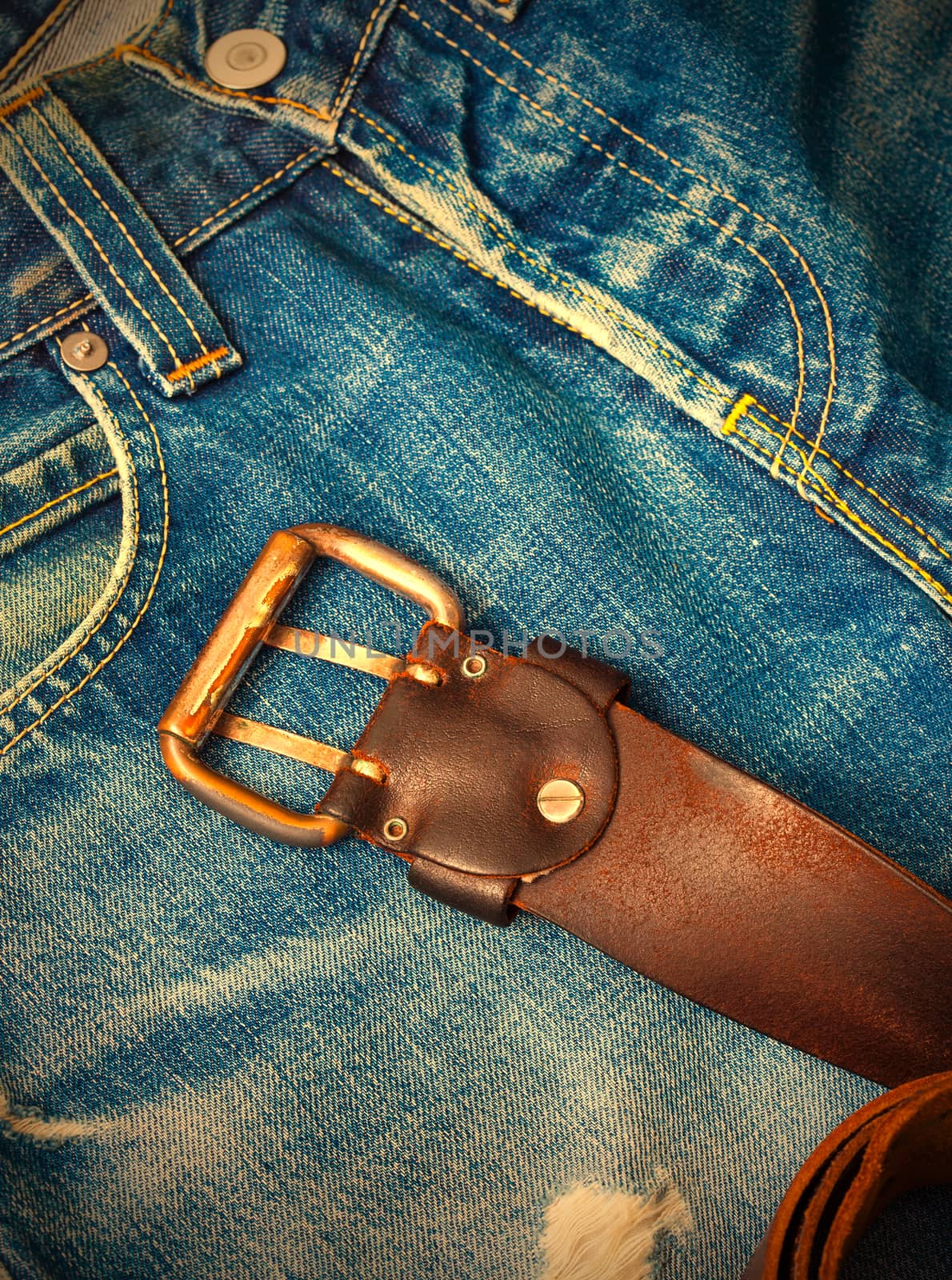 Vintage leather belt with a buckle lying on old jeans with a hole. instagram image retro style