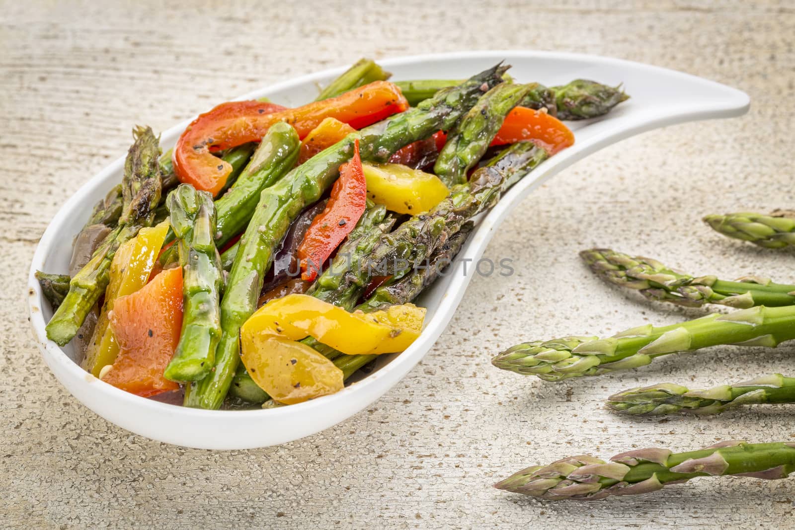 roasted asparagus salad on a teardrop shaped bowl against white painted rustic wood with fresh asparagus