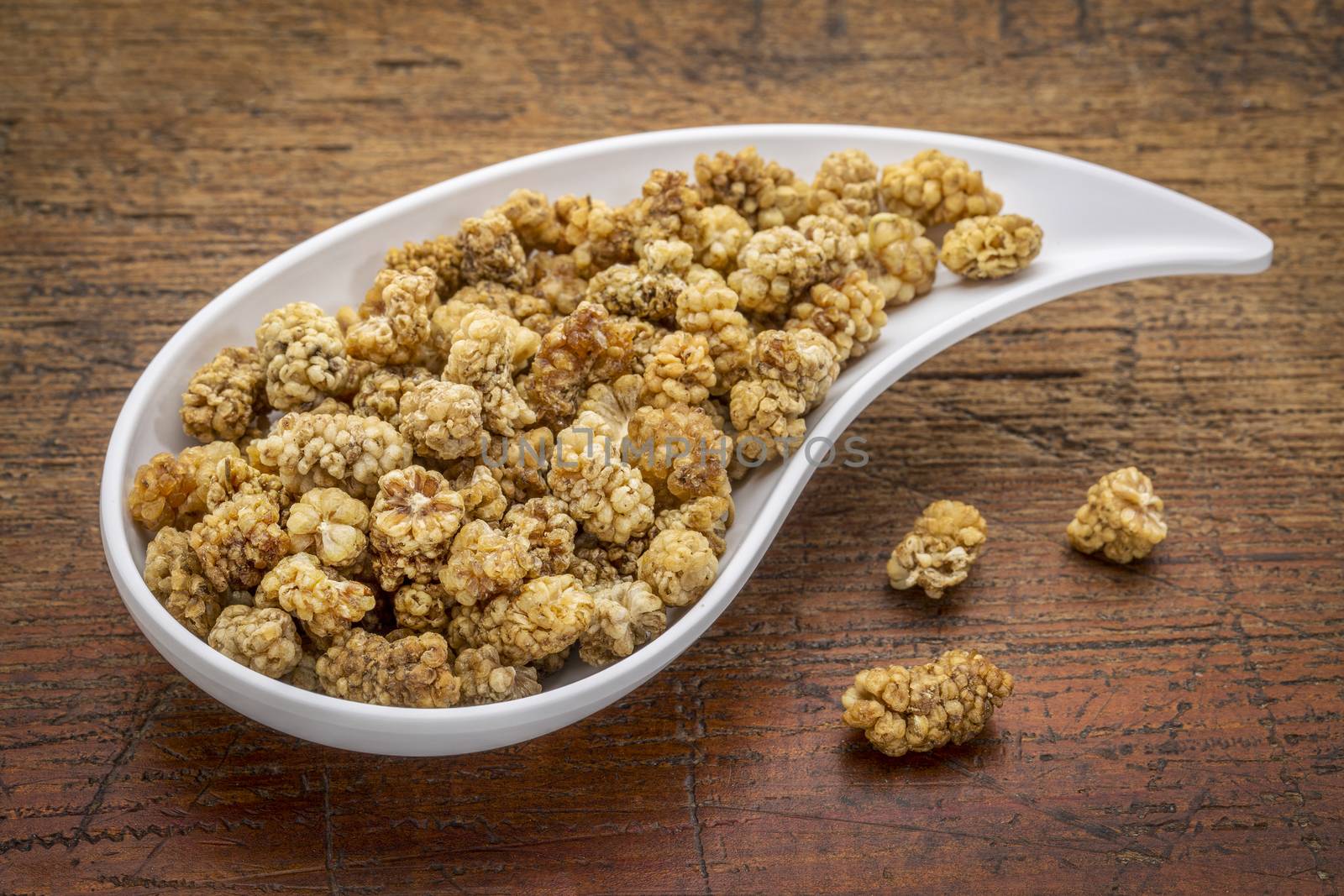 dried white mulberry on a teardrop shaped bowl against rustic wood