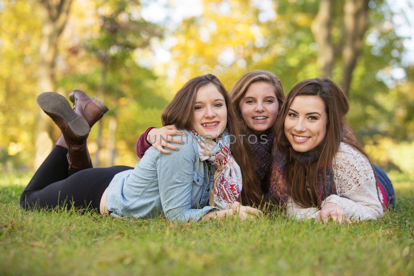 Trio of happy teen girls laying down on grass