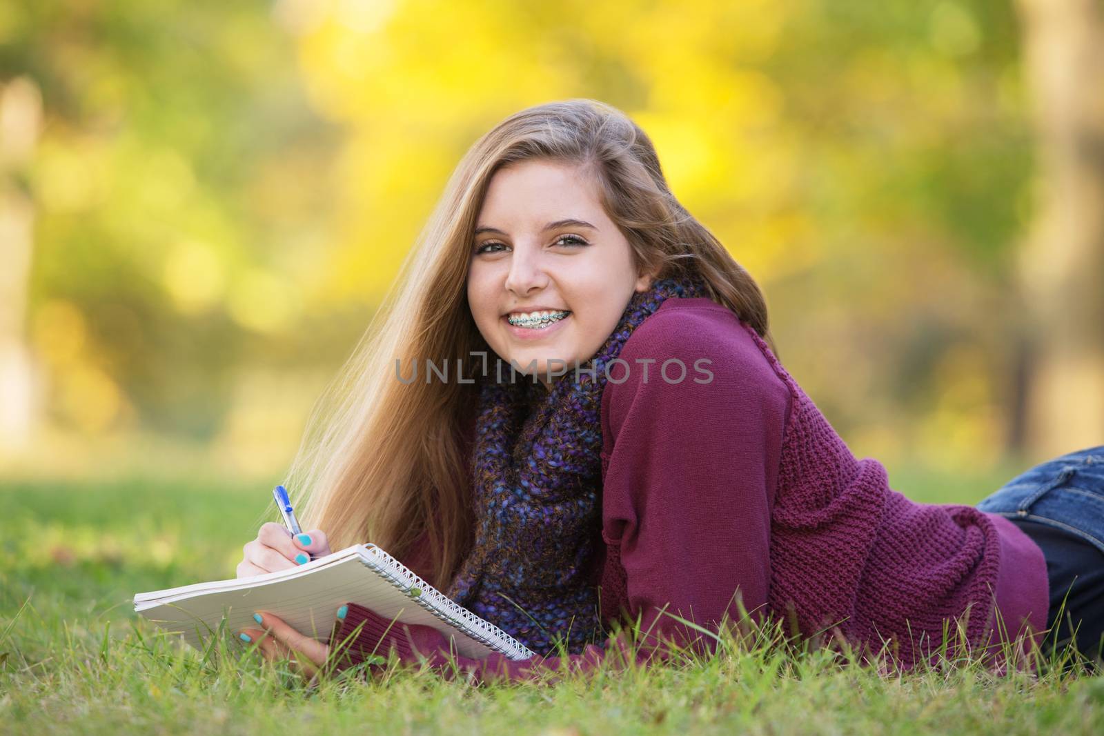 Female teen with braces taking notes while laying on ground