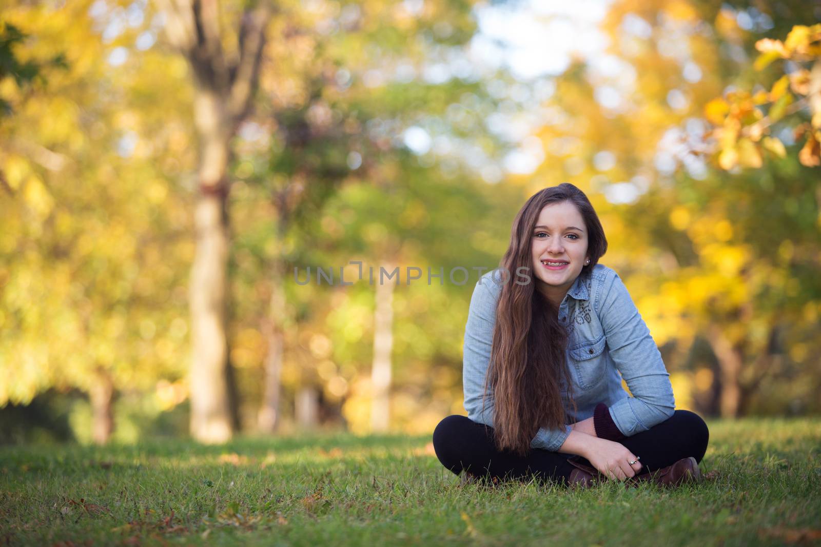 Cheerful single female teenager sitting outdoors on grass