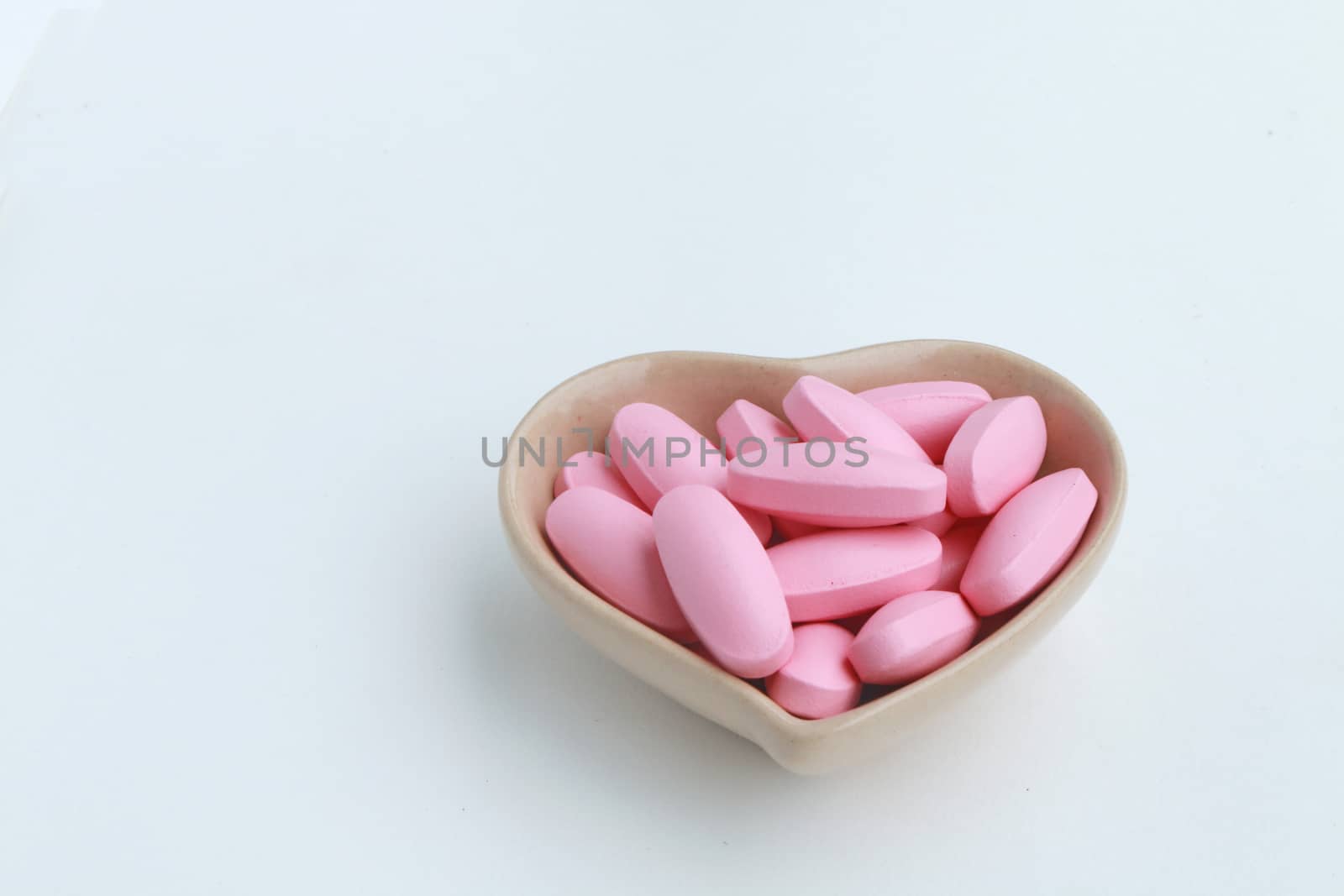 Many pink oval pills in the ceramic cup shape of heart.