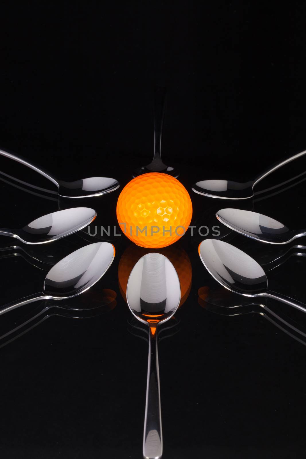 Teaspoons and orange golf ball on the black glass table  by CaptureLight