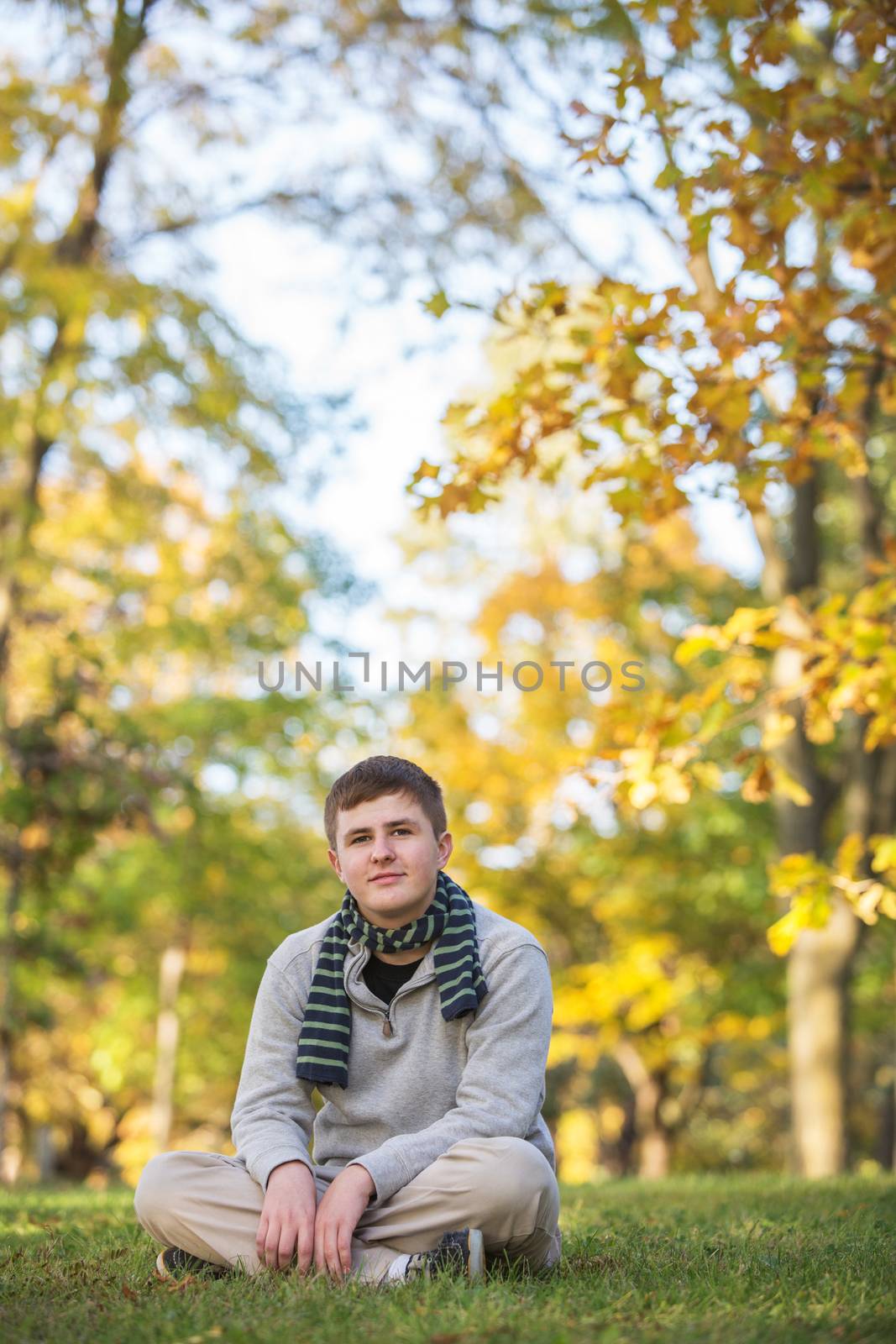 Calm Caucasian teenager sitting on grass during the  autumn season