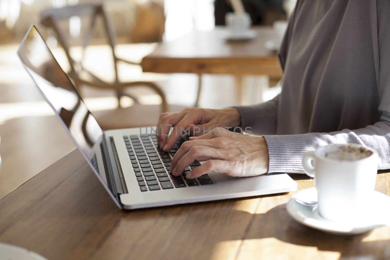 brunette mauve sweater woman typing keyboard pc laptop with white small cup cappuccino coffee on light brown wooden table cafe