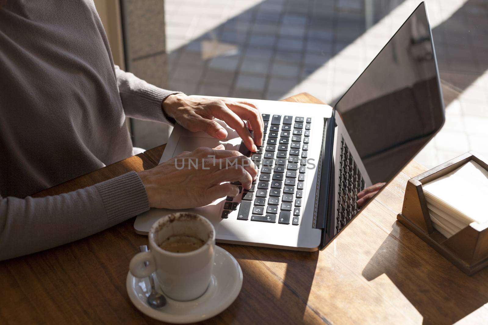 brunette mauve sweater woman typing keyboard pc laptop with white small cup cappuccino coffee on light brown wooden table cafe