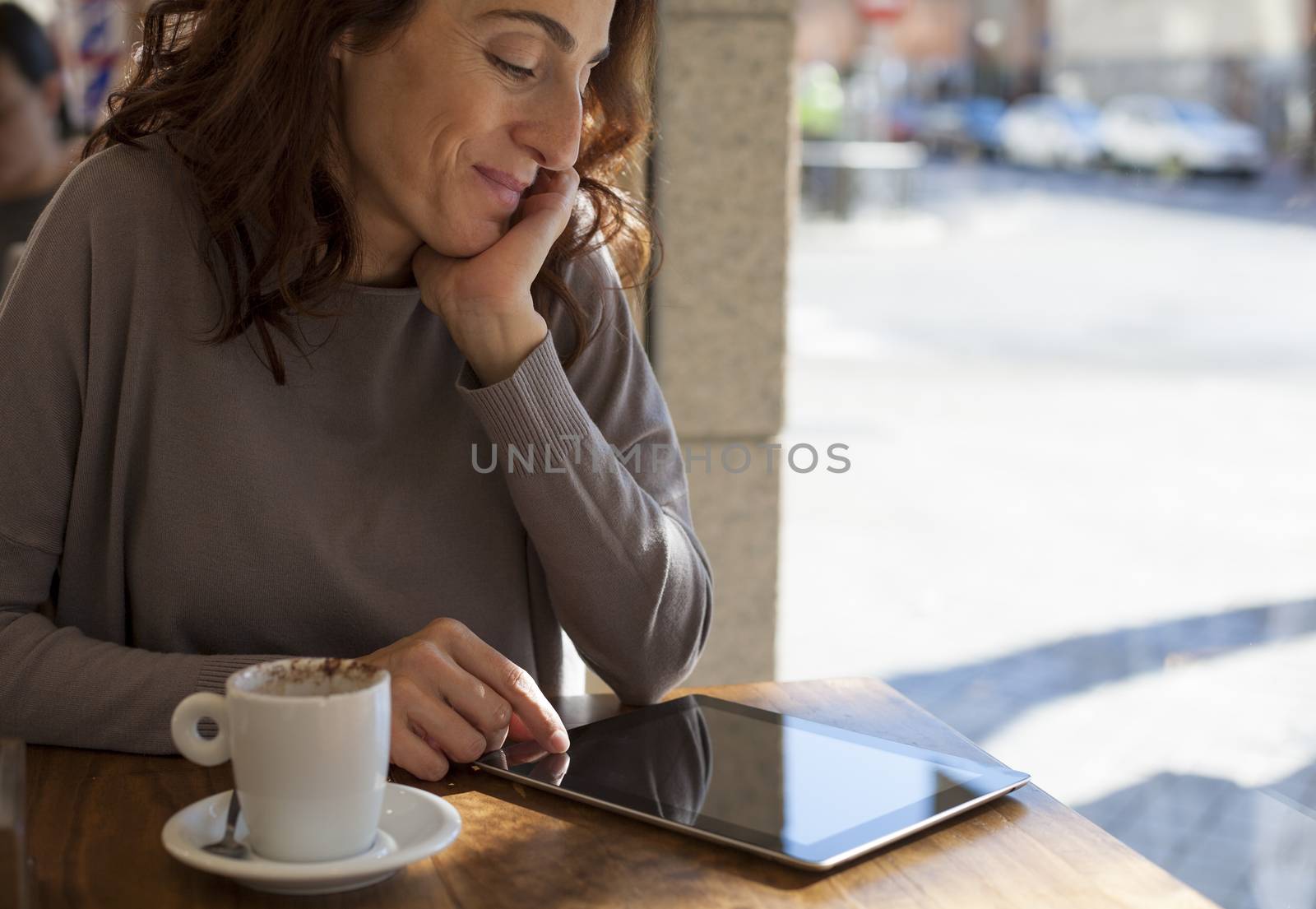 woman touching digital tablet blank screen with white small cup cappuccino coffee on light brown wooden table cafe
