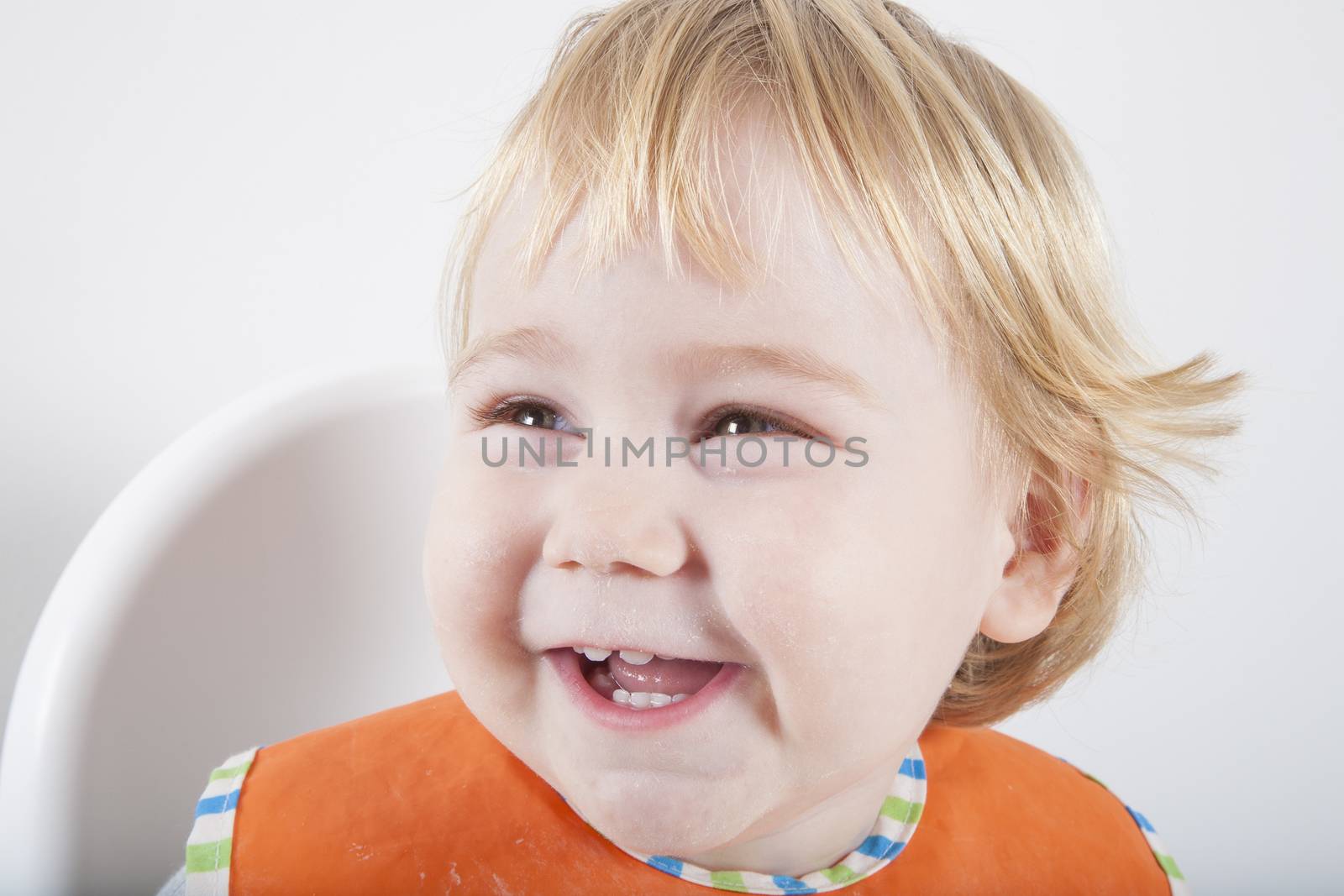 blonde caucasian baby seventeen month age orange bib grey sweater on white high chair laughing looking