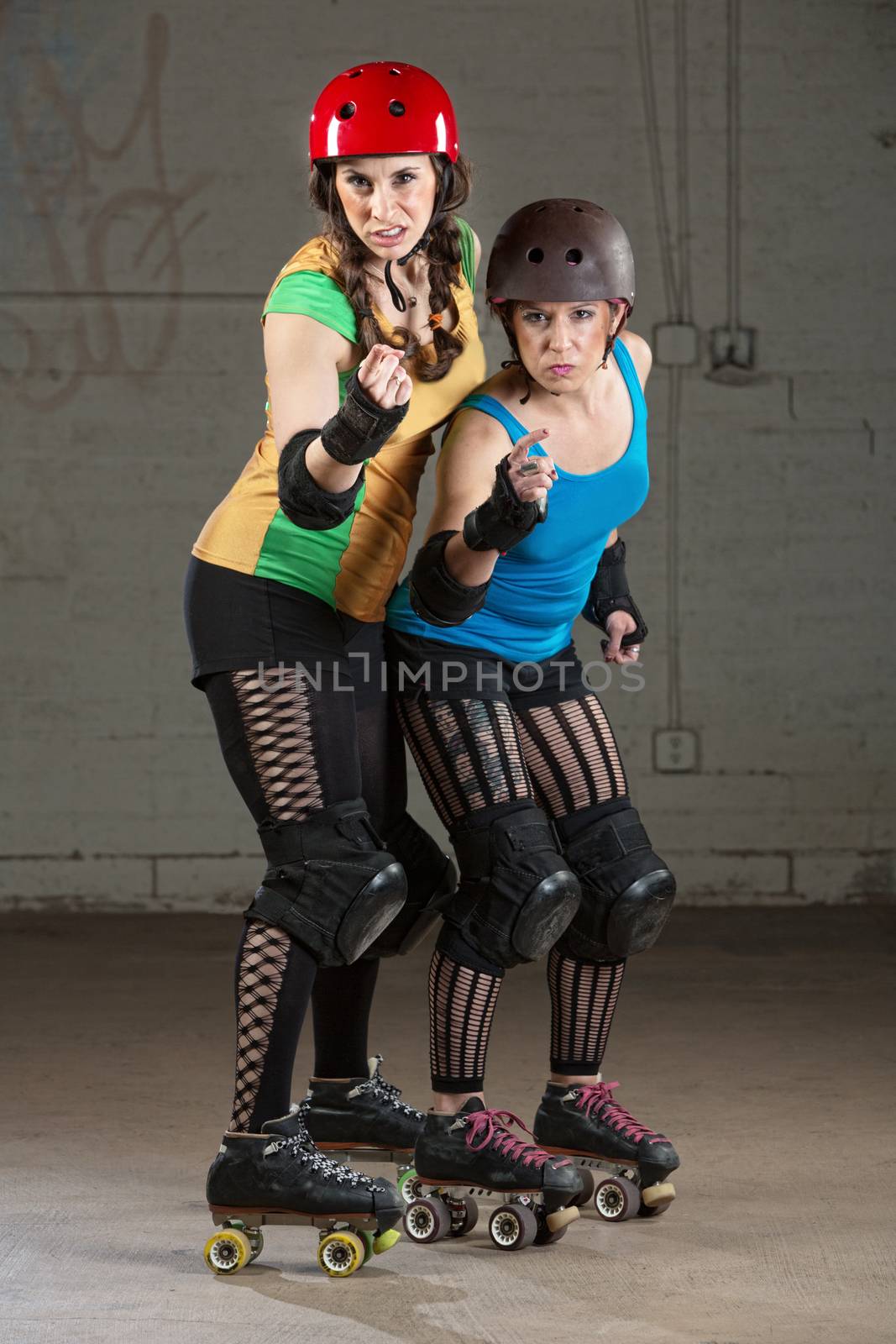 Female roller derby skaters in helmets pointing and shaking fists