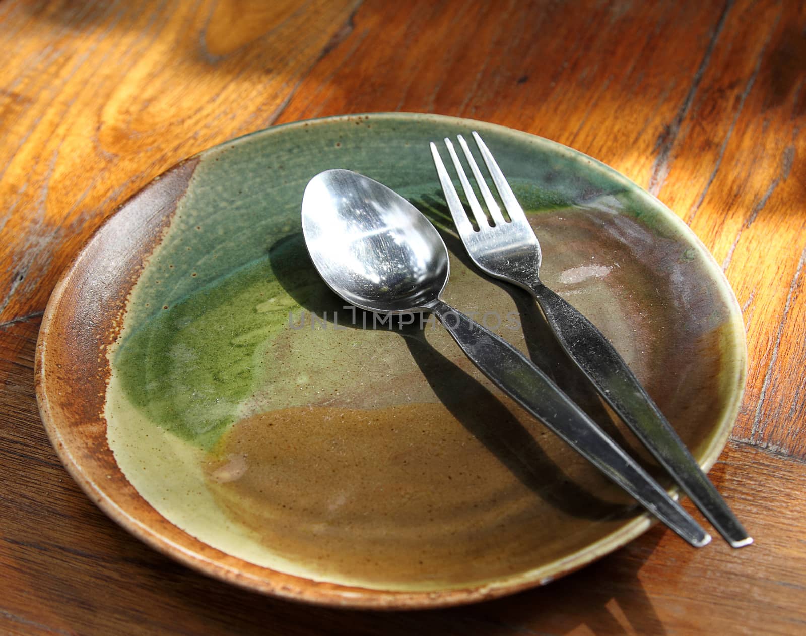 Empty plate with spoon and fork on wooden table