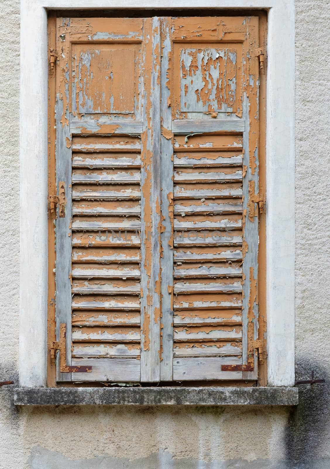 Closed window of the old building covered by wooden blinds with peeling paint