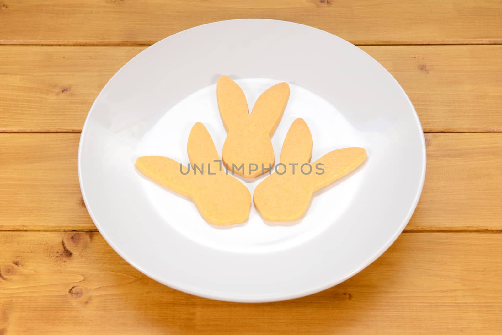 Three rabbit-shaped biscuits for Easter on a white plate on a wooden table