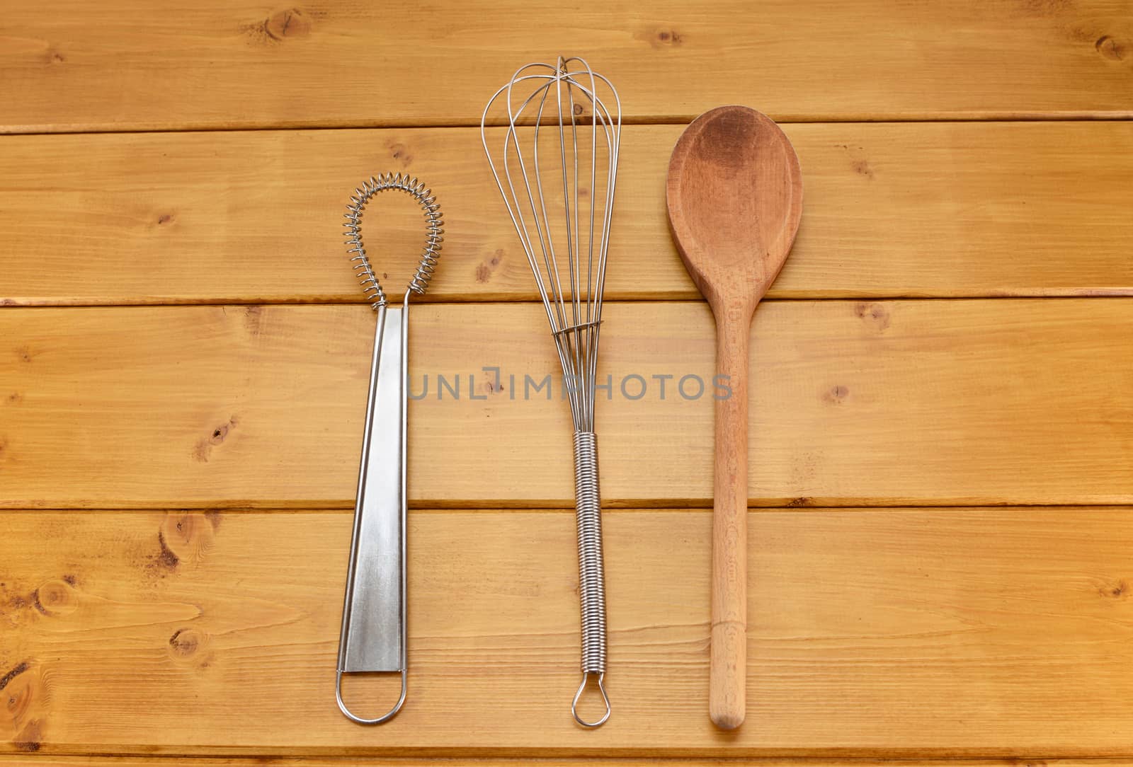 Sauce and balloon whisks and wooden spoon on a kitchen table