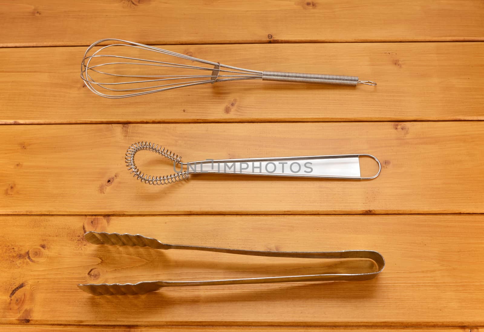 Balloon and sauce whisks and metal tongs on a wooden table