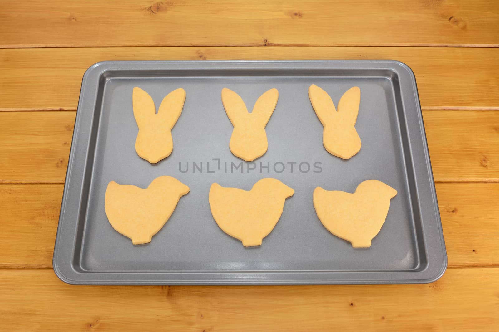 Baking tray with six Easter cookies - bunnies and chicks - on a wooden table
