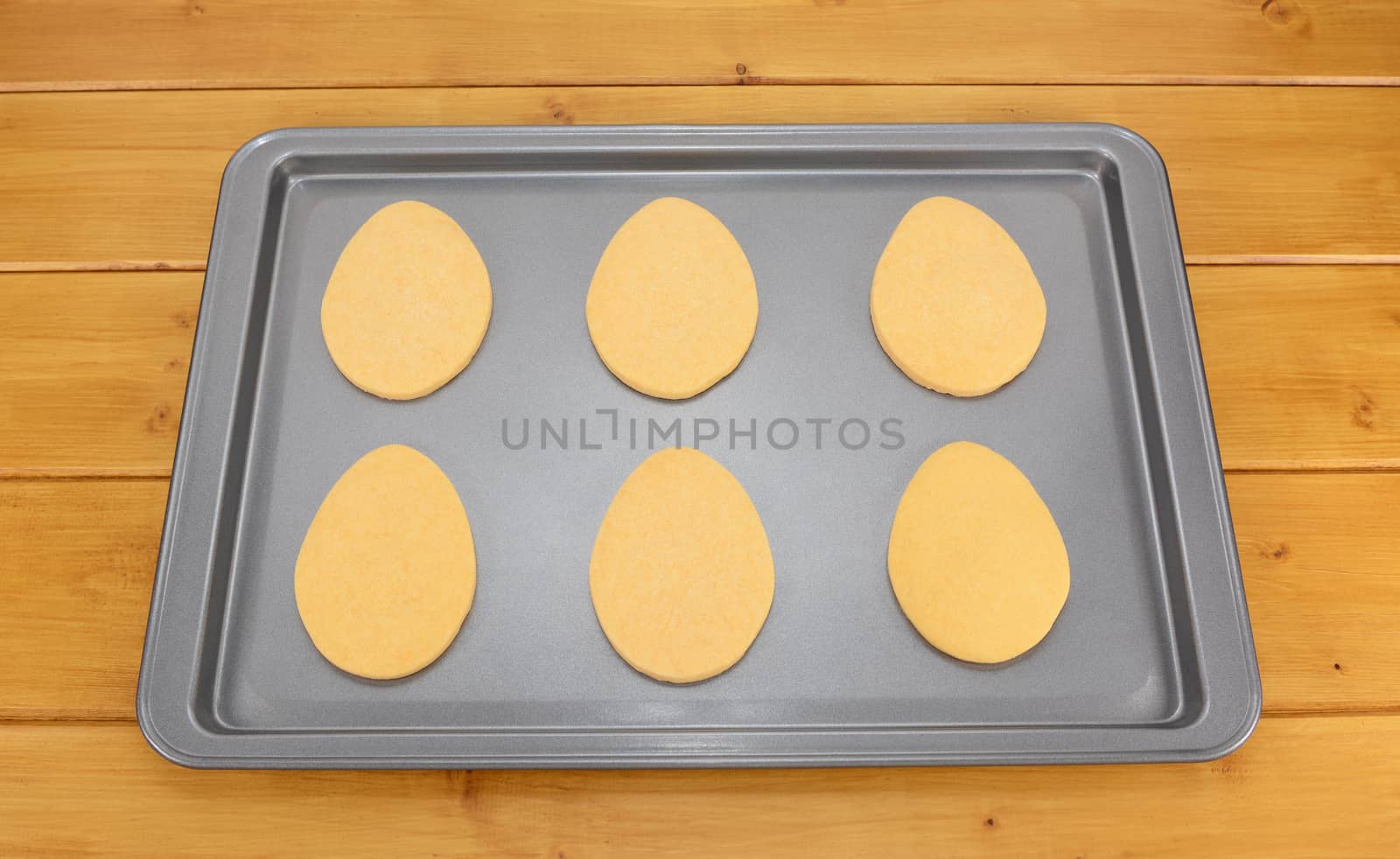 Six egg shaped Easter cookies on a baking tray on a wooden table