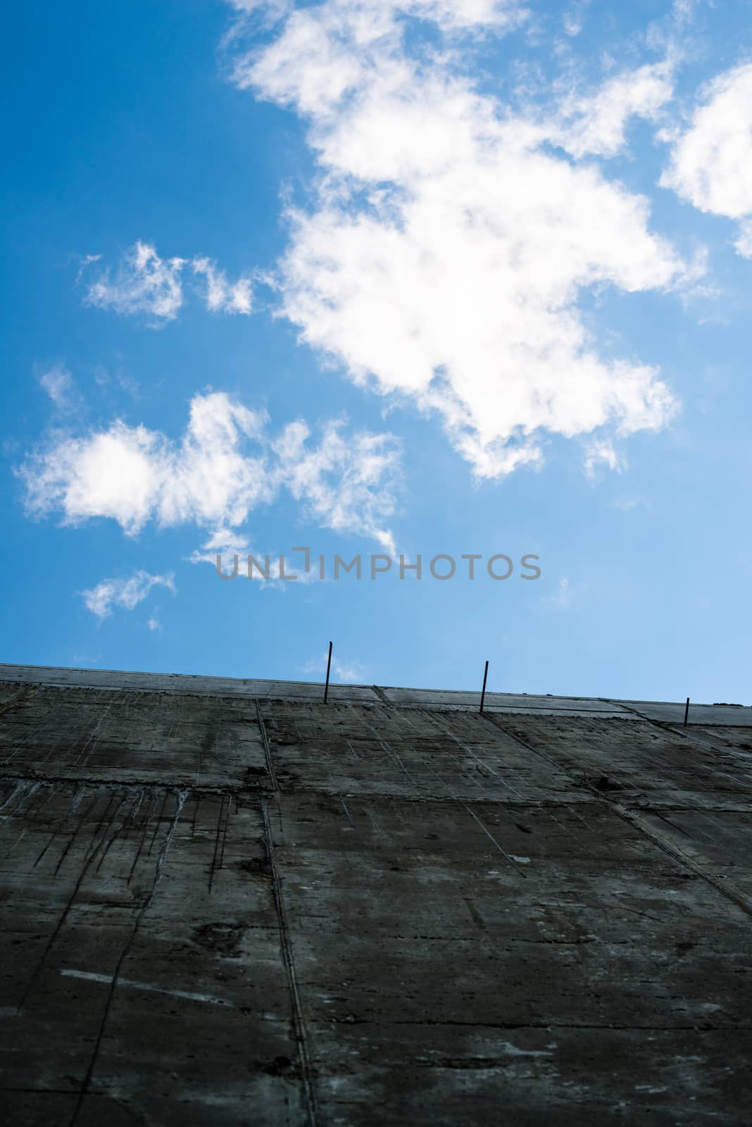 Gray concrete wall against the blue sky with white clouds.