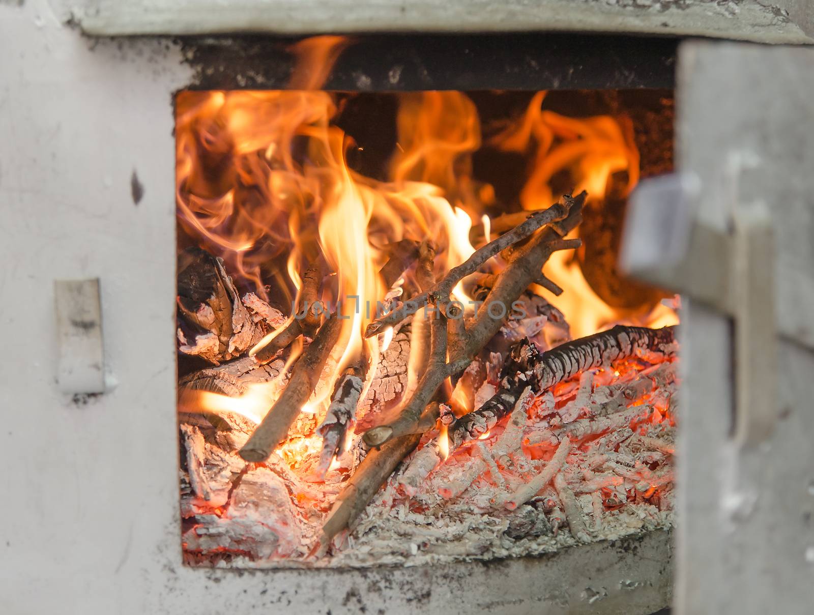 Distillation still Pot chamber fire-place burning wood branches with open door, detail with selective focus