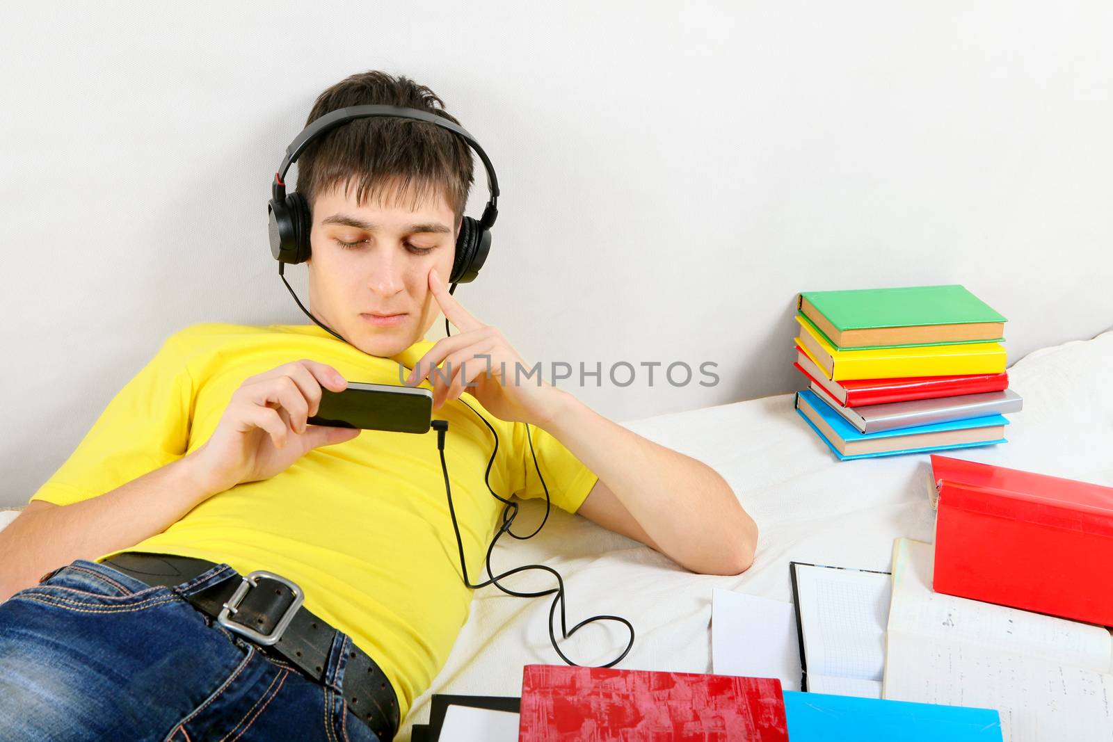 Bored Student in Earphones with the Books on the Bed