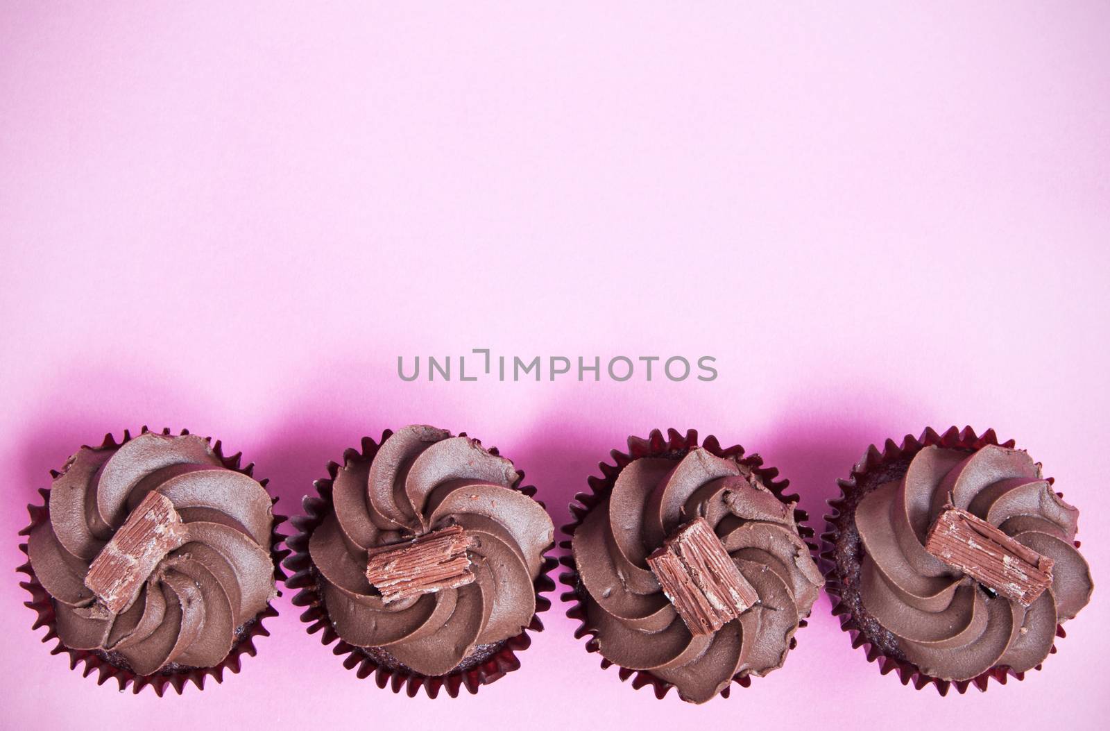 Chocolate cupcakes creating a border over a pink background