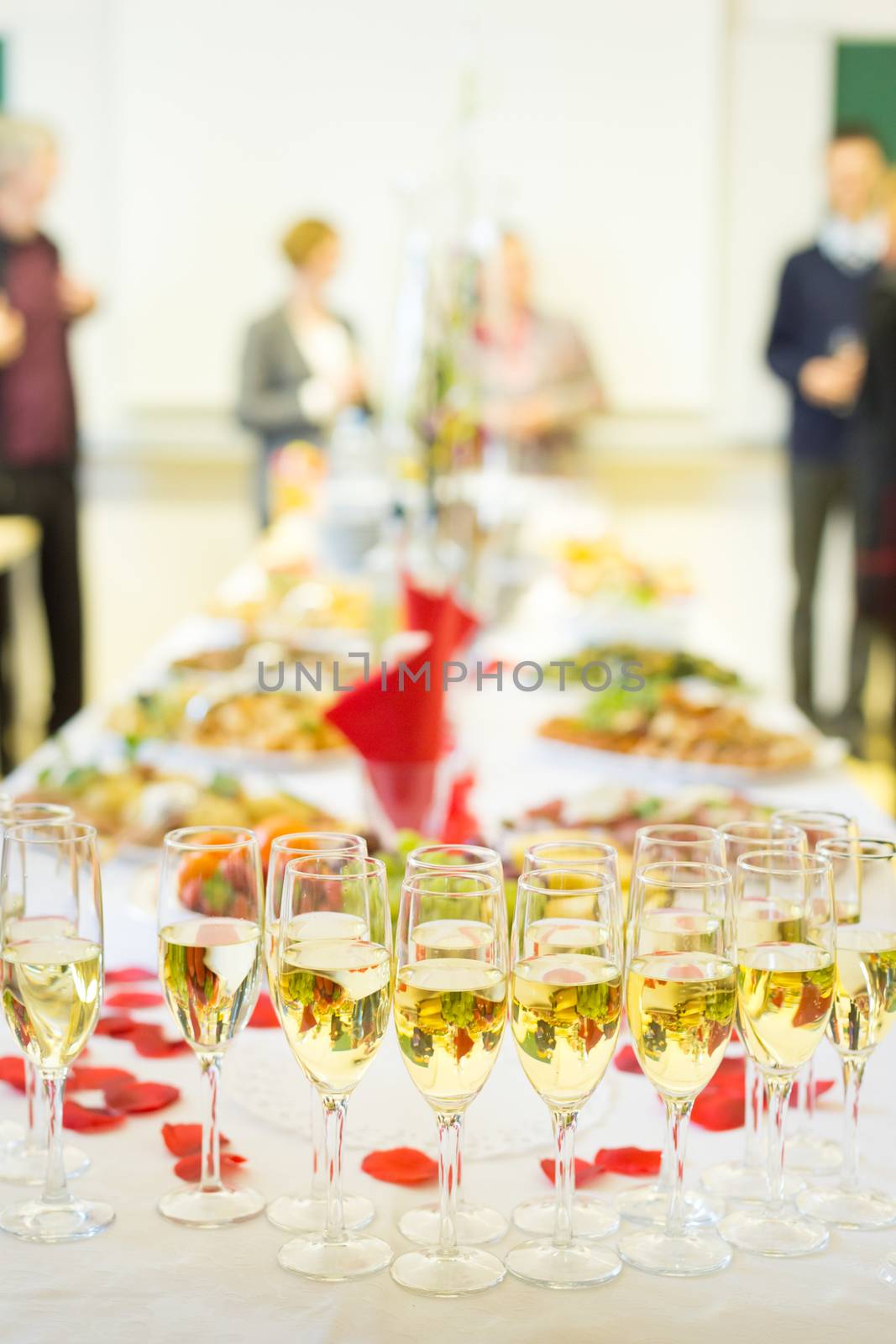 Banquet event. Table with the wineglasses, snacks and cocktails. People celebrating in the background.