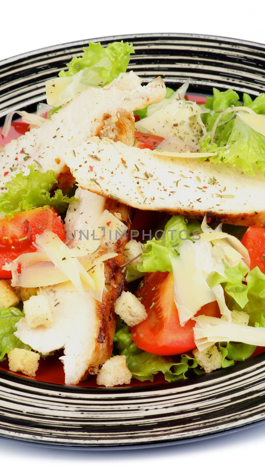 Caesar Salad with Grilled Chicken Breast, Garlic Crouton, Lettuce, Tomatoes and Grated Parmesan Cheese on Striped Plate closeup on white background