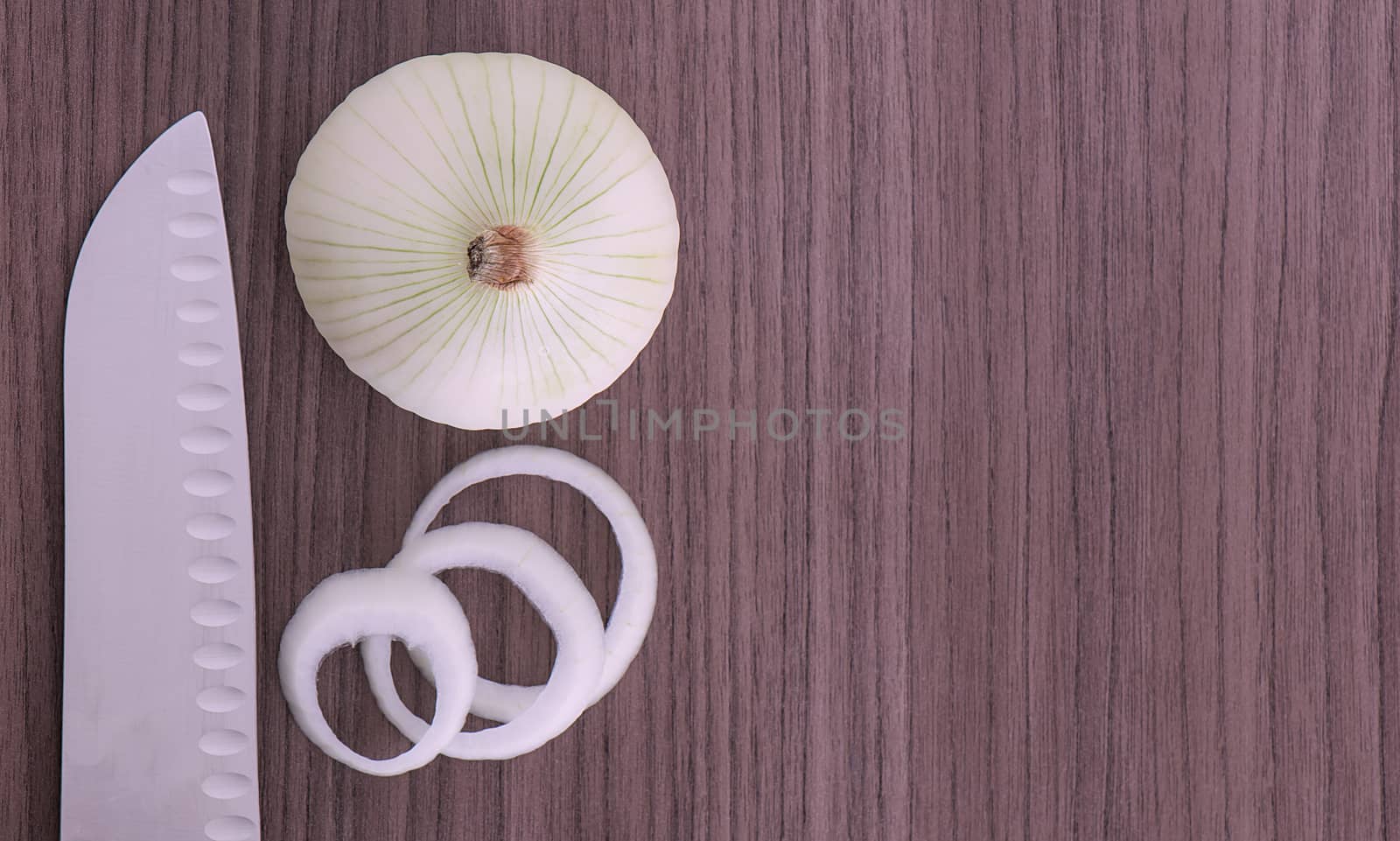 A knife and an onion with some onion rings 